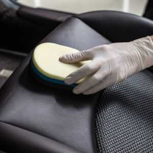 A person in gloves cleaning the seat of a car.