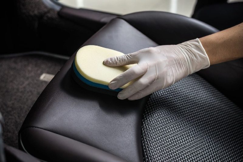A person in gloves cleaning the seat of a car.