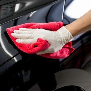 A person cleaning the side of a car with red cloth.