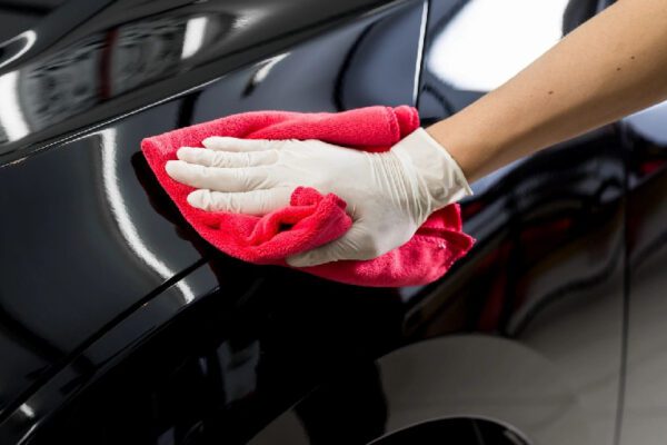 A person cleaning the side of a car with red cloth.