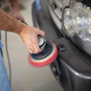 A person is using a polisher to clean the bumper of a car.