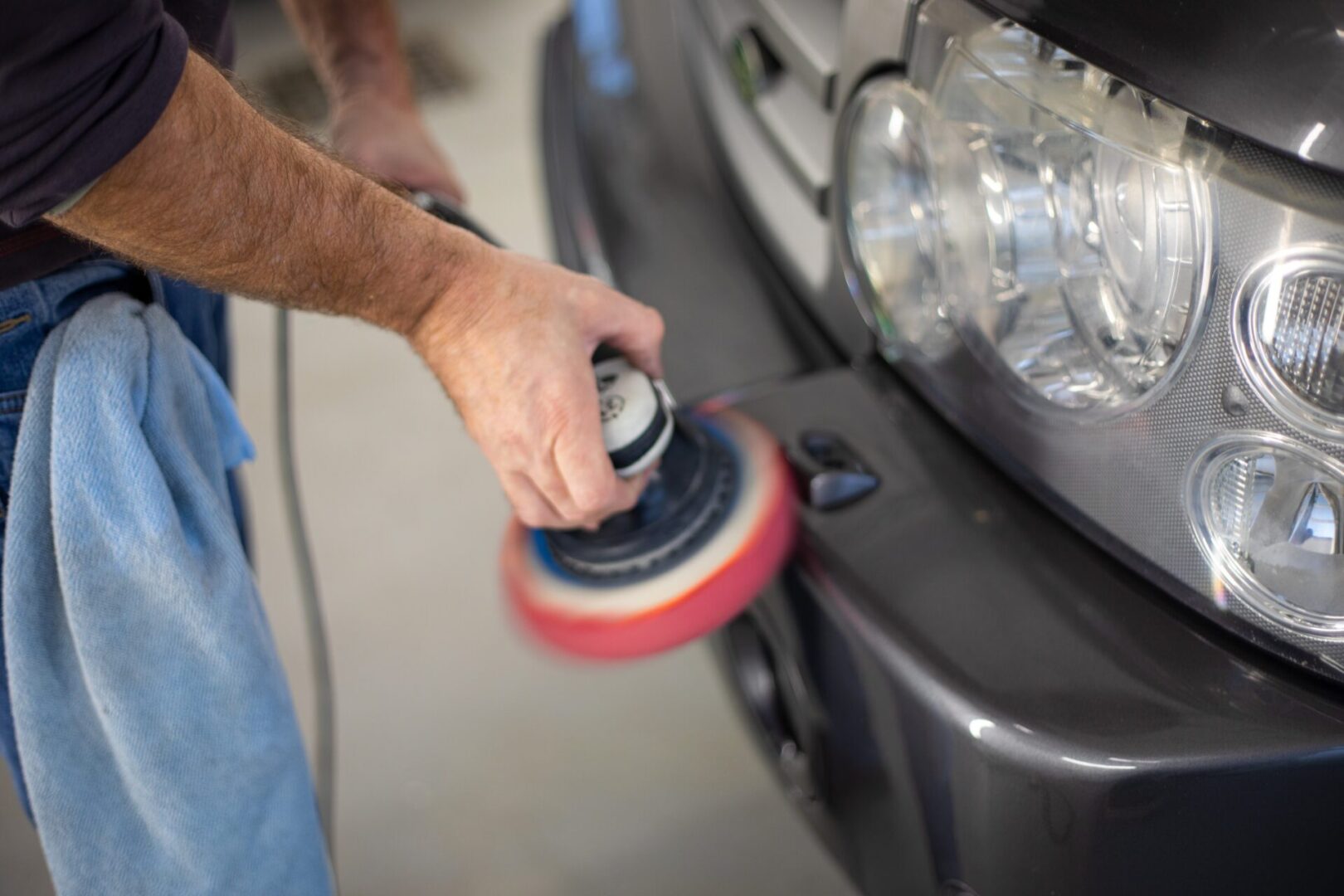 A person is using a polisher to clean the bumper of a car.