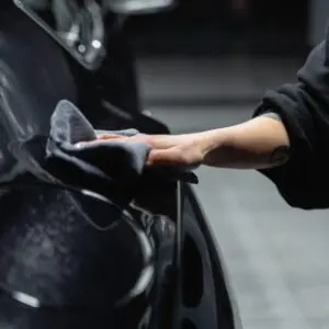 A person cleaning the side of a car with a cloth.