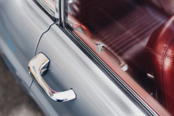 A silver door handle and window on a car.