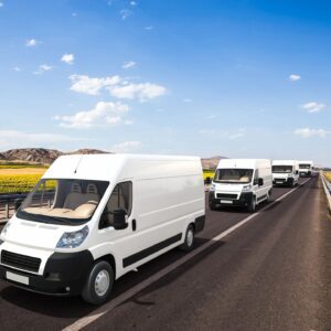 A line of white vans driving down the road.